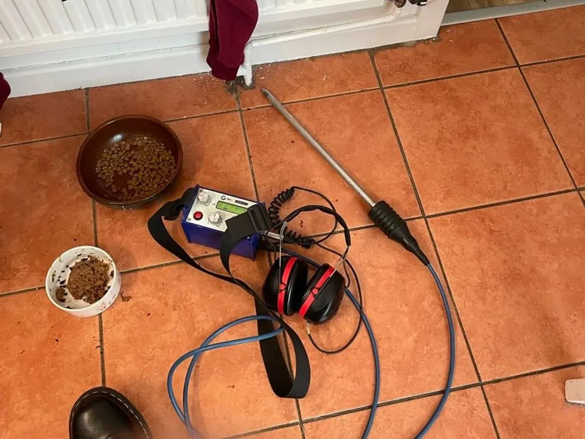 Listening stick, amplifier and ear defenders laid on terracotta kitchen tiles beneath a radiator