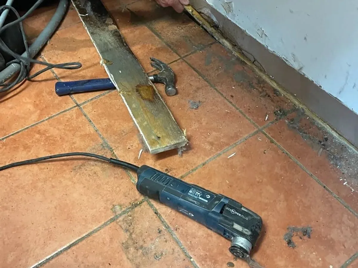 Kitchen floor tiles lifted and ground dug out against the wall, exposing the heating pipes and tee in wet soil