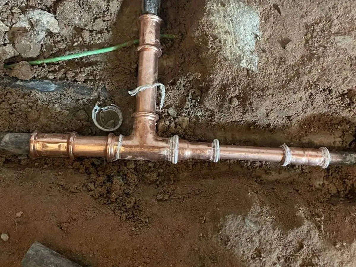 New copper tee and pipe joined with press fittings, lying in the dug-out floor