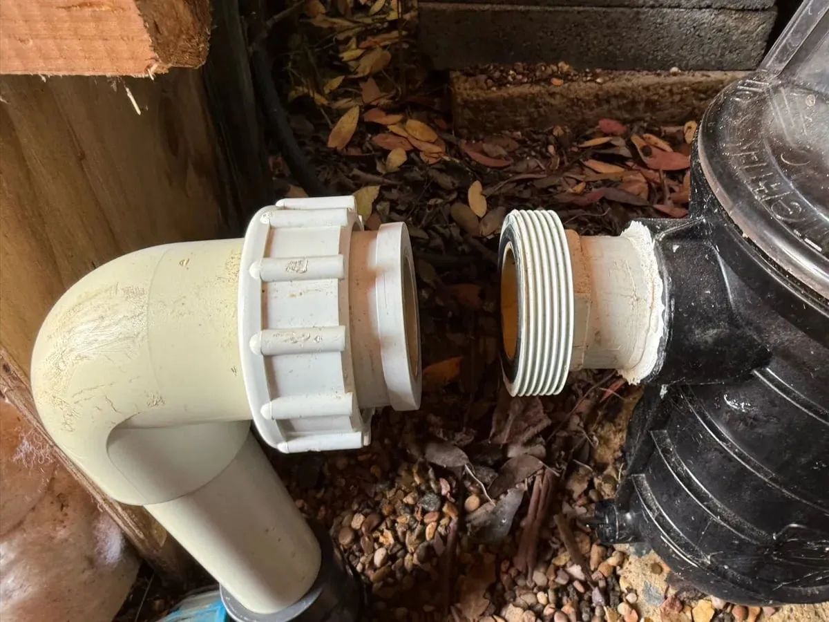 Cream pool pipe elbow and union disconnected from a black pump, showing the joint where the leak was found