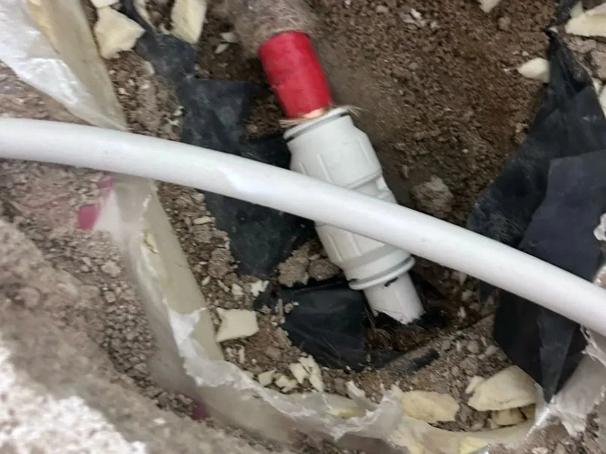 White plastic heating pipe joined with a push-fit coupling in the opened floor, with red sleeving on the pipe behind
