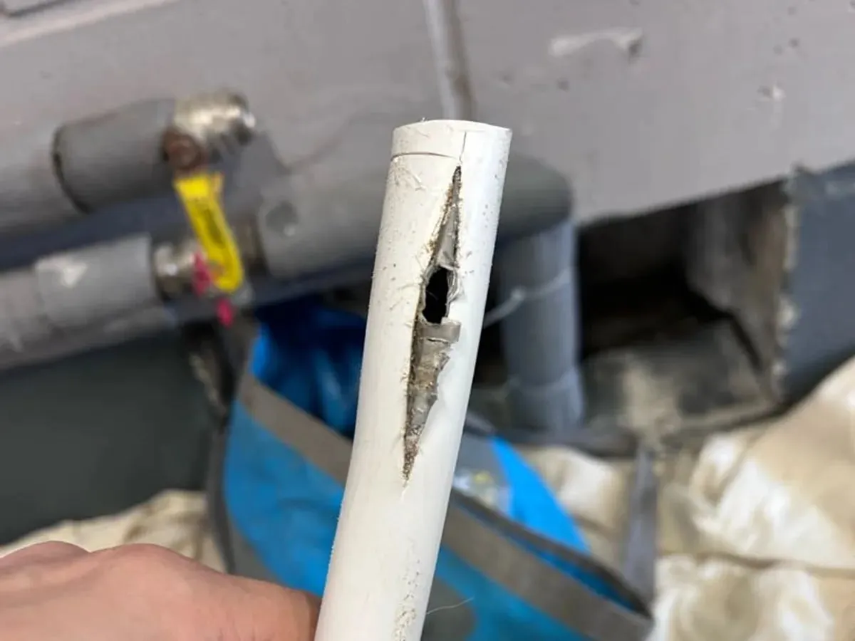 Hand holding a cut length of white plastic heating pipe with a long split in its side