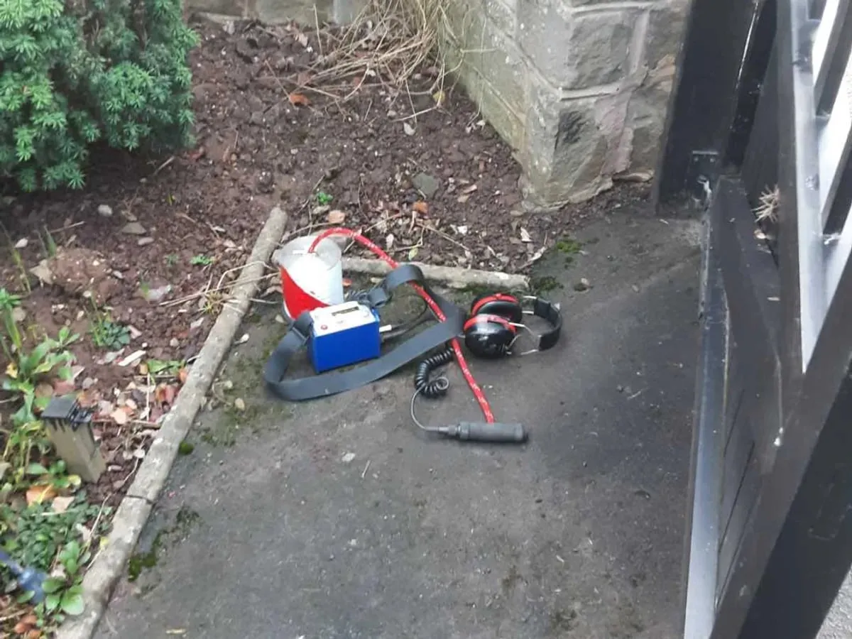 Red and white ground microphone, blue amplifier and ear defenders on a path by a garden border and a black gate