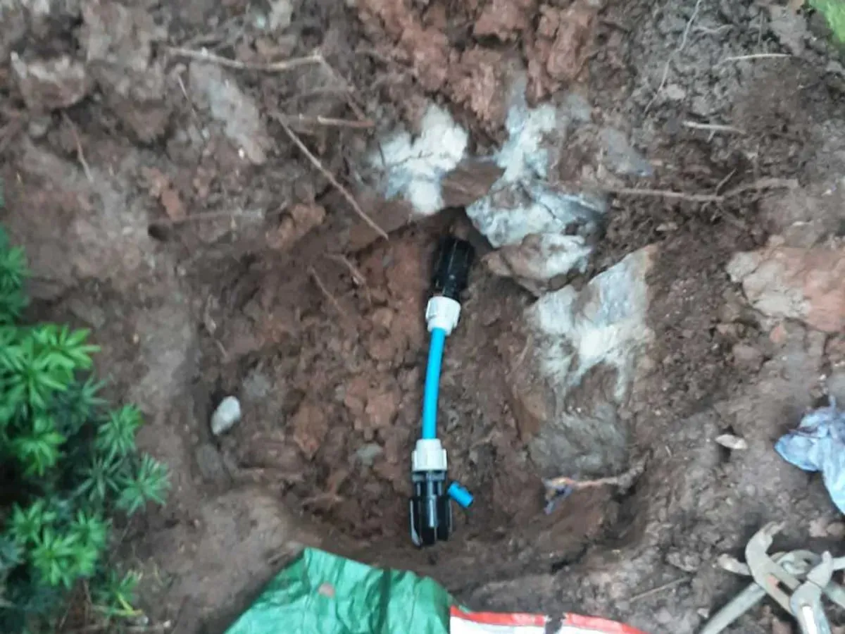 Short length of blue MDPE pipe joined with black couplings in a hole in the garden soil