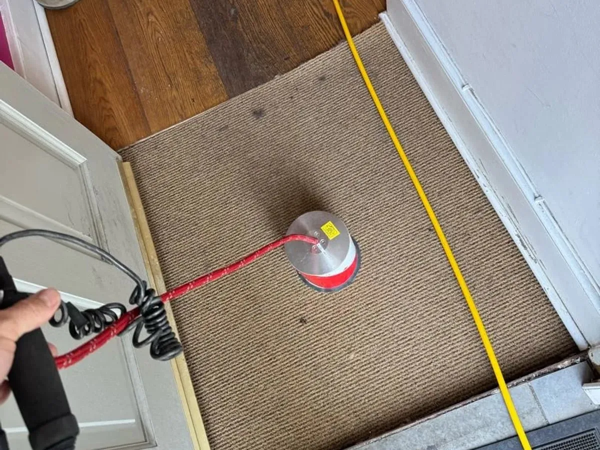 Silver and red ground microphone on a doormat inside a front door, with the engineer holding its handle
