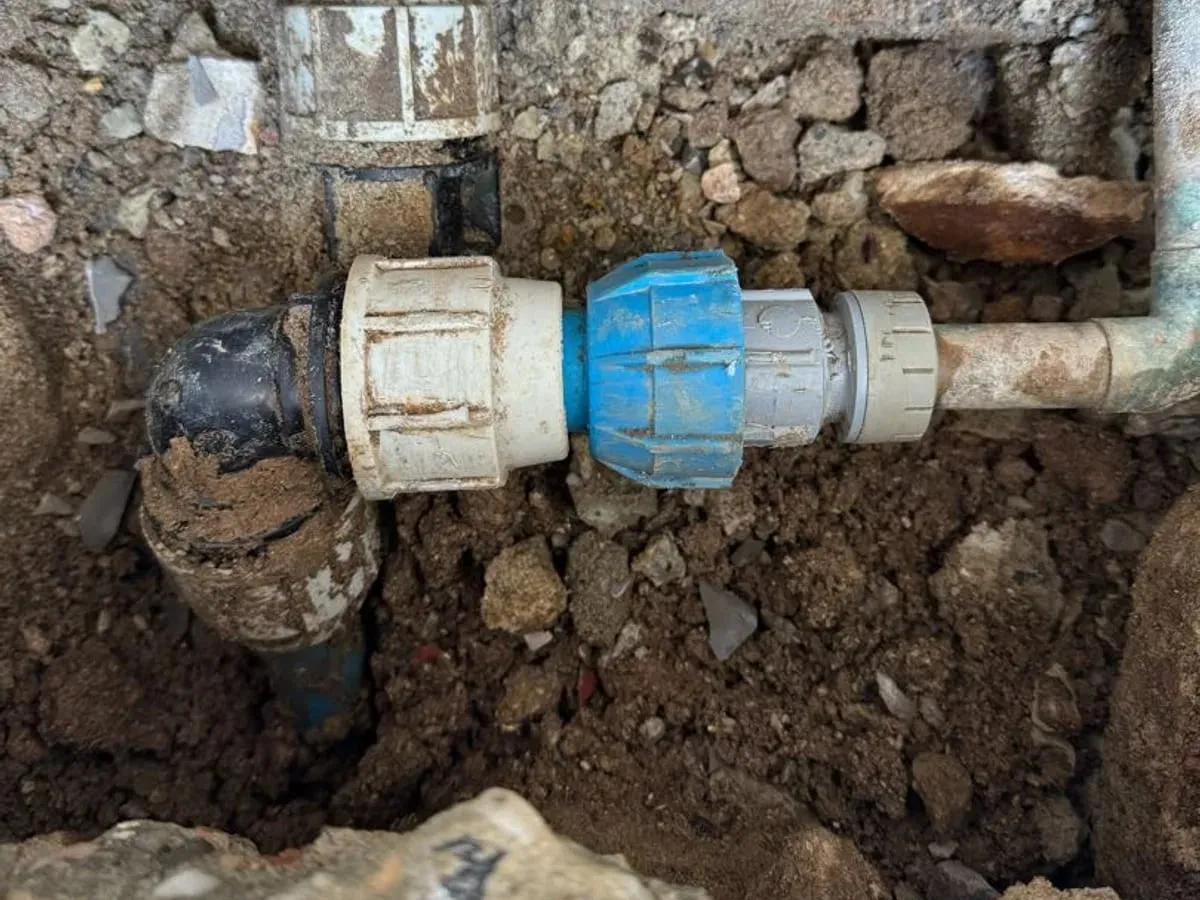 New white and blue compression fittings on the supply pipe in the dug-out ground under the step