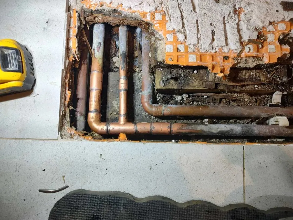 Opened section of tiled floor showing copper pipes running through the channel after repair