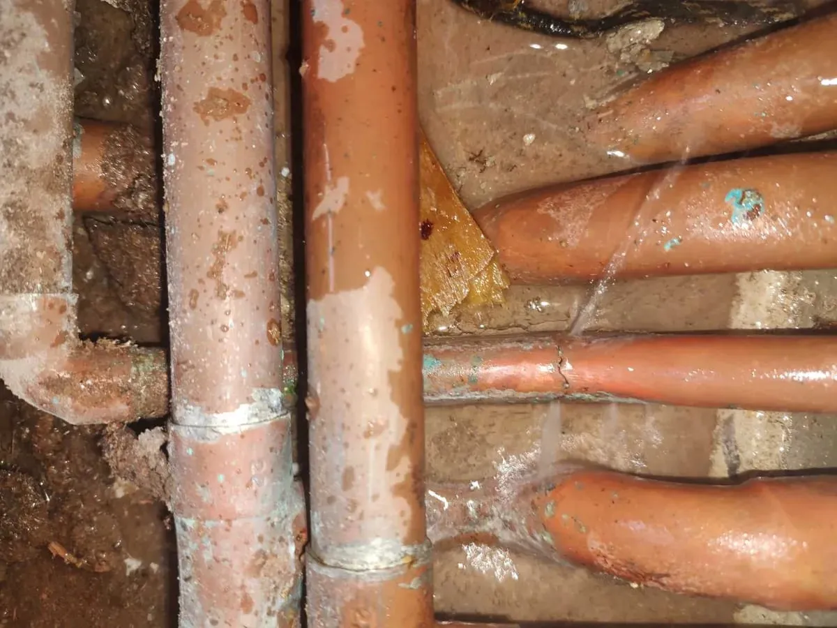 Wet copper pipes under the floor with a fine spray of water coming from a joint